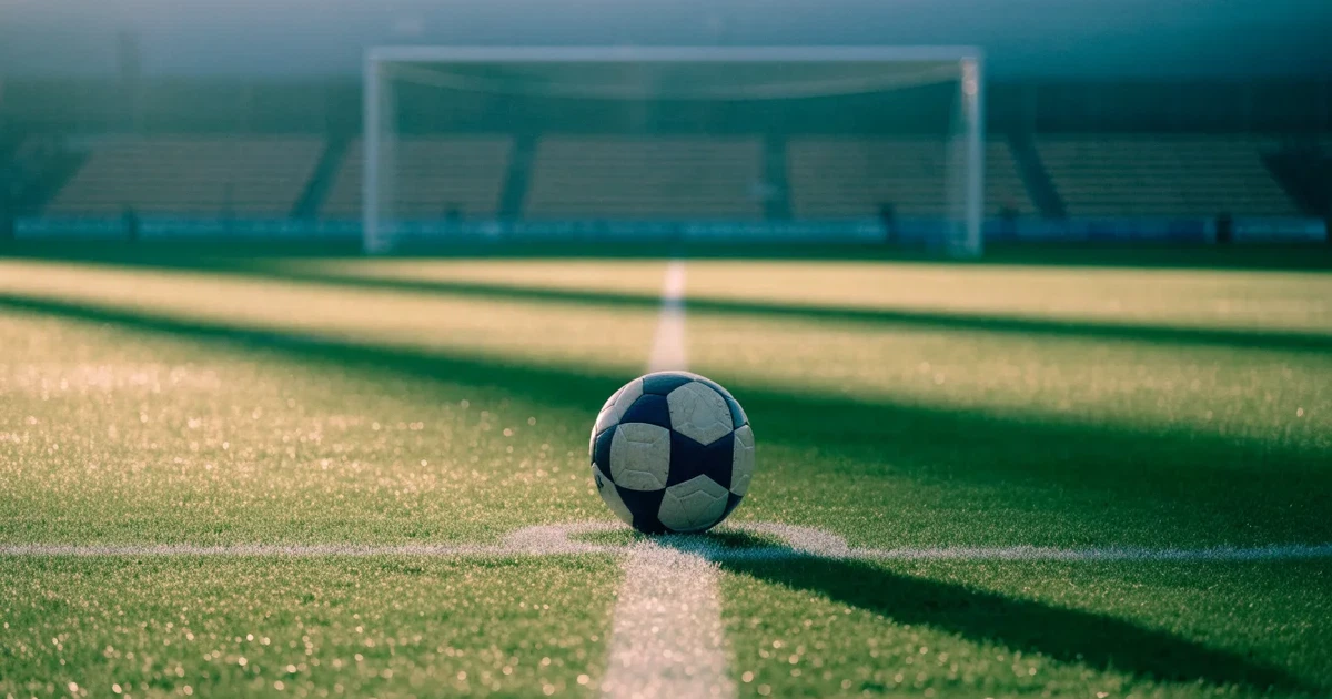 Un pallone da calcio sul dischetto del centrocampo di un prato, alla luce del mattino