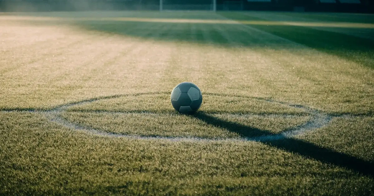 Un pallone da calcio sul dischetto del centrocampo di un prato, alla luce del mattino